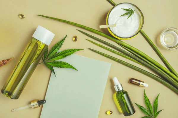 Cosmetics with hemp CBD oil on a beige background, notebook, marijuana leaves. Copy space, mockup — Stock Photo, Image