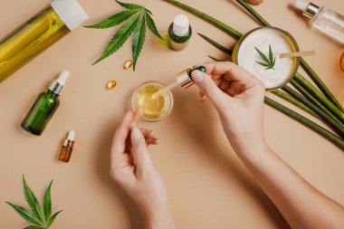 CBD kozmetik yağlı bir boru, kadın ellerinde kozmetik ürünler, esrar ve kenevir yapraklı krem, marihuana