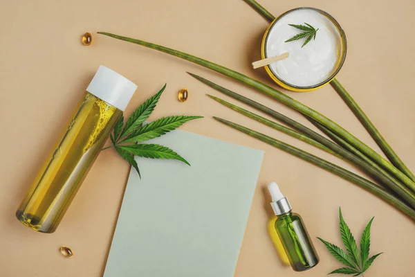 Cosmetics with hemp CBD oil on a beige background, notebook, marijuana leaves. Copy space, mockup — Stock Photo, Image