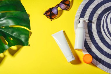 Güneş kremi. Sarı arka planda güneş gözlüklü ve koruma kremi sürgülü şapka vardı. Plaj aksesuarları. Yaz Konsepti
