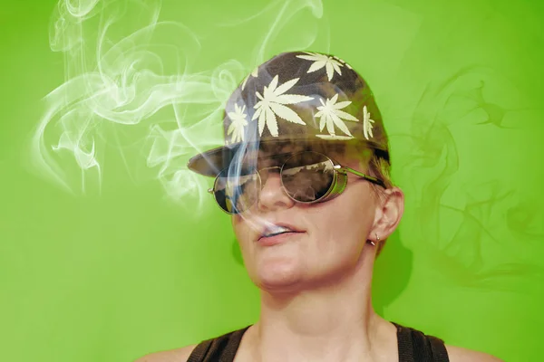 Meisje met zonnebril en pet met bladeren van marihuana rookt op gele achtergrond — Stockfoto