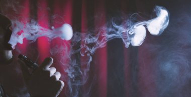 genç adam vaping bulutlar karanlık bir arka plan üzerinde.