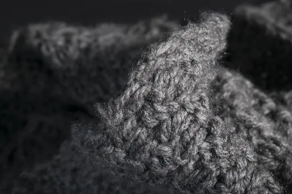 Isolated handmade knitted gray fabric on a dark background.