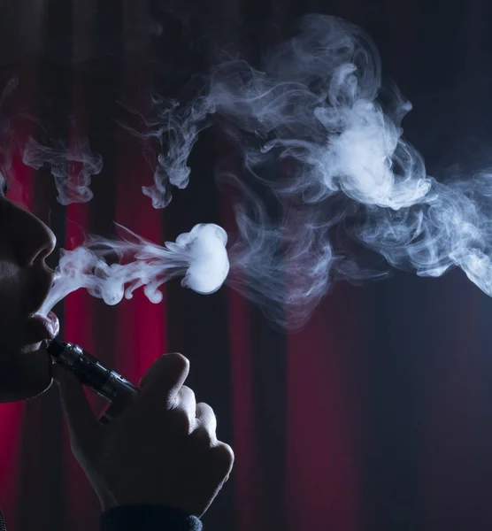 Ecigarette o cigarrillo electrónico con nubes sobre un fondo oscuro . — Foto de Stock