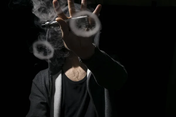 Giovane uomo in possesso di sigaretta elettronica e facendo vaping trucchi . — Foto Stock