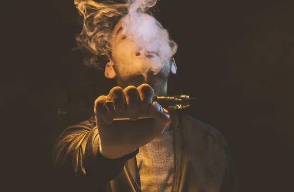 Isolated man vaping e cigarette over a dark background — Stock Photo, Image