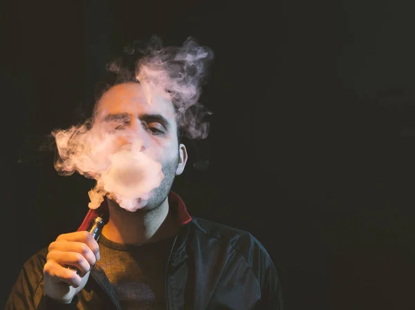 Geïsoleerde man vaping e sigaret op een donkere achtergrond — Stockfoto