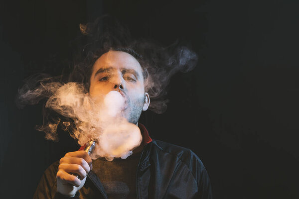 isolated man vaping e cigarette over a dark background