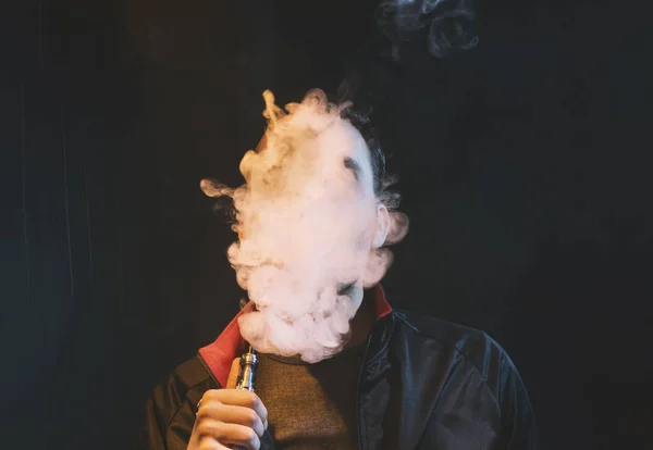 Geïsoleerde man vaping e sigaret op een donkere achtergrond — Stockfoto