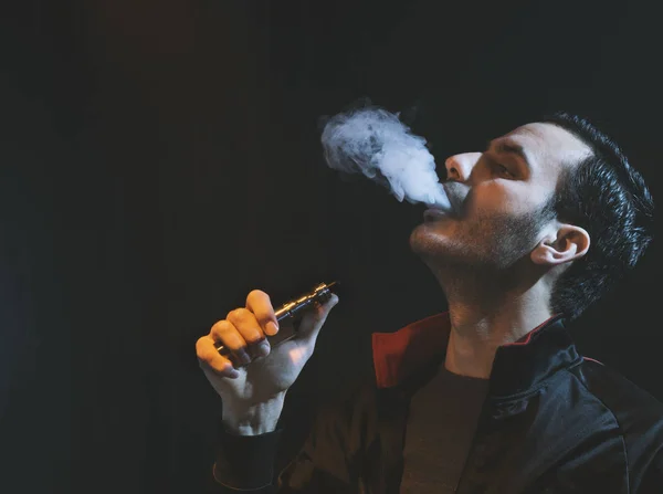 Isolierter Mann verdampft E-Zigarette vor dunklem Hintergrund — Stockfoto