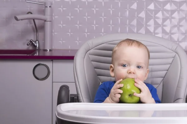 Смешной мальчик с большим зеленым яблоком на кухне — стоковое фото