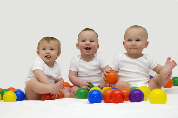Trigémeos de bebê rindo e brincando com bolas coloridas — Fotografia de Stock