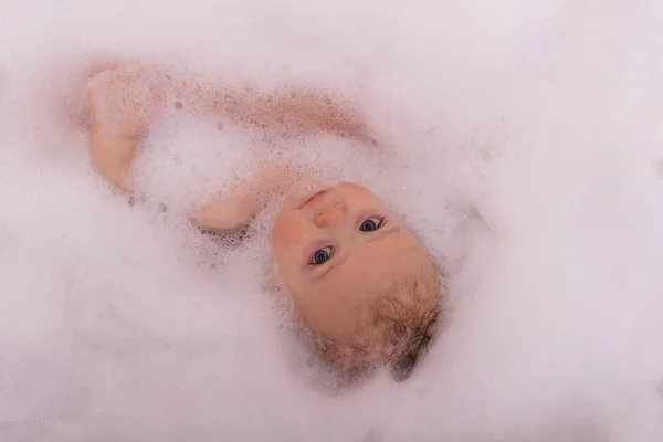 Un bebé en una bañera en espuma de jabón mirando a la cámara —  Fotos de Stock