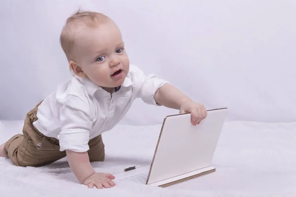Симпатичный вдумчивый мальчик в белой рубашке играет с планшетом. Смешной мальчик с ноутбуком похож на маленького бизнесмена. — стоковое фото