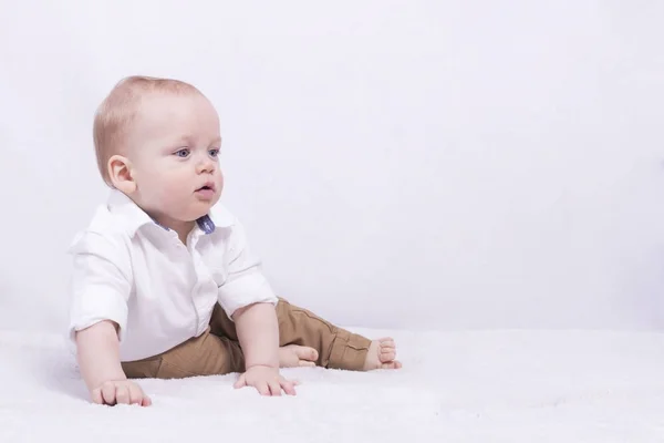 Thoughful big-eyed småbarn tittar bort och sitter på det vita täcket. Kopiera utrymme. Formulär för ett vykort — Stockfoto