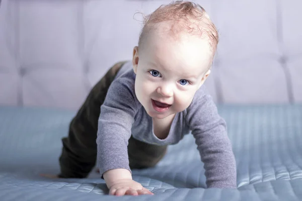 Un niño arrastrándose mirando la cámara. Un niño sonriente en la cama. Niño de boca abierta en su habitación. —  Fotos de Stock