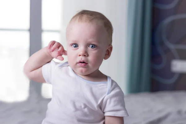Toddler chłopiec drapanie za uchem i patrząc na kamery. Blue-eyed spokojny niemowlę noworodek. Close-up portret — Zdjęcie stockowe