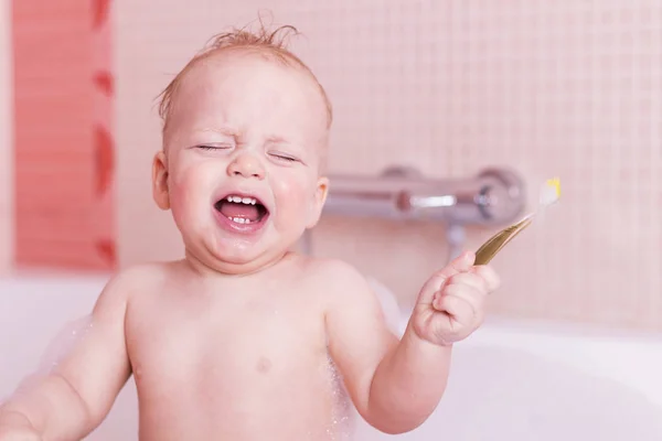 Плаче хлопчик, який миє зуби зубною щіткою. Немовля з зубною щіткою у ванні — стокове фото