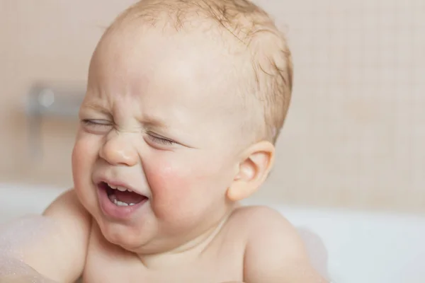 Crying baby by in a bathtub. Infant kid sreaming while taking a bath