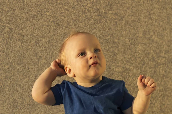 Thoughtful infant boy sitting against the wall and looking away. Posing toddler boy with unusual shadows on his face — Stock Photo, Image