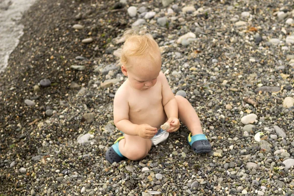 Grave bambino si siede sulla spiaggia di pietra e guardando il tramonto — Foto Stock