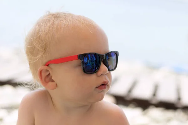 Grave bambino carino in occhiali da sole sulla spiaggia . — Foto Stock