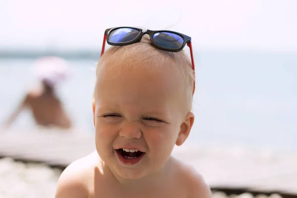 Amusant tout-petit riant dans des lunettes de soleil sur la mer. Petit patron en vacances — Photo