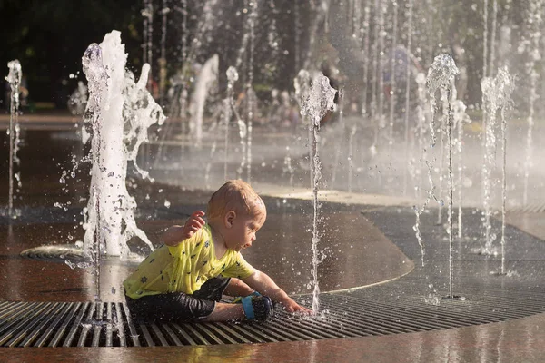Смешной мальчик плескается в фонтан. Милый малыш играет с водяным потоком — стоковое фото
