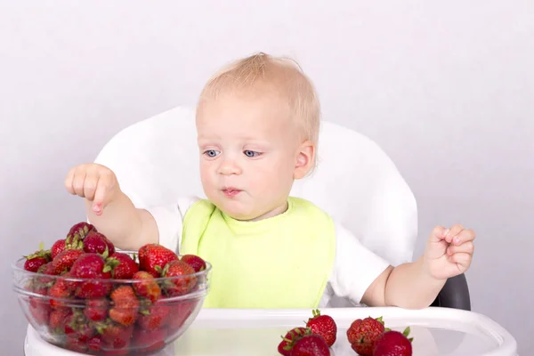 Blue eyed funny toddler choosing strawberries. Cute baby boy eating strawberries