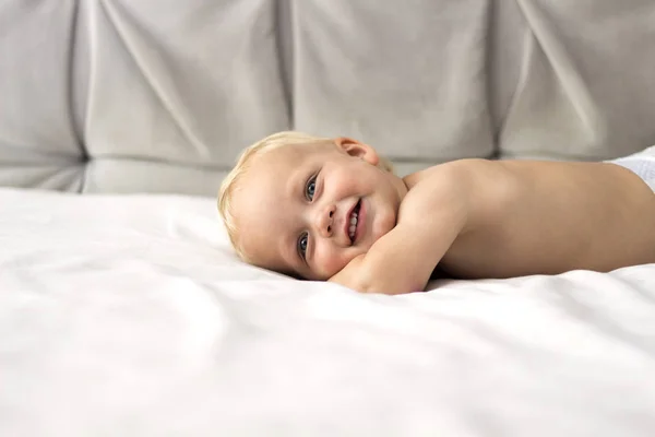 Lindo niño sonriente acostado en la cama sobre el fondo gris. Copiar espacio —  Fotos de Stock