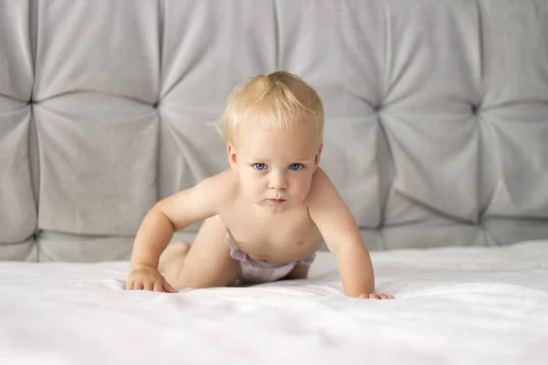Seriuos niño arrastrándose en la cama. Niño concentrado en la manta blanca —  Fotos de Stock