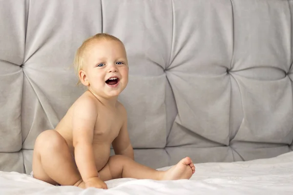 Adorable niño oloroso sentado en la cama sobre el fondo gris. Copiar espacio —  Fotos de Stock