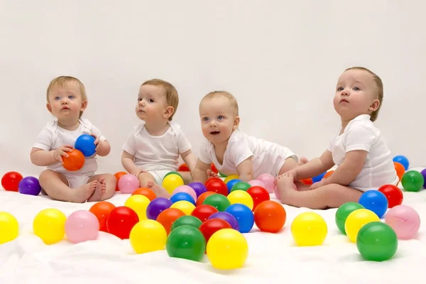 Четыре милых смешных младенца сидят на белом одеяле и играют красочные шары. Детская вечеринка . — стоковое фото