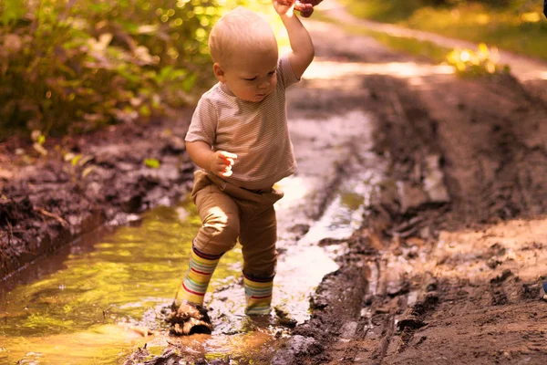 Смешной мальчик в резиновых сапогах веселится в лесной луже — стоковое фото