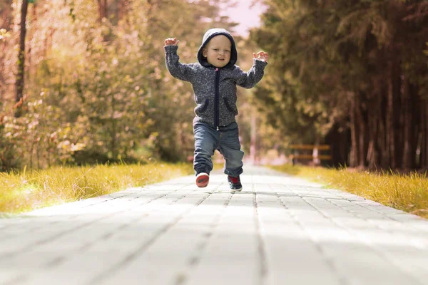 Смешной малыш в капюшоне бегает и прыгает в осеннем переулке — стоковое фото