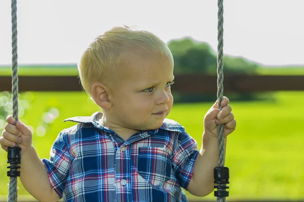 Милый малыш на качелях на открытом воздухе. Портрет очаровательного мальчика, играющего на детской площадке — стоковое фото
