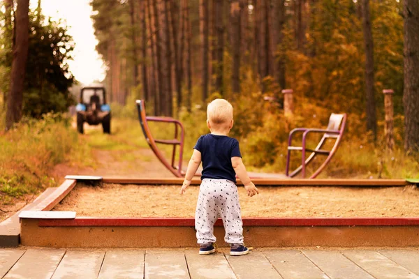 Тоддлер на детской площадке смотрит на размытый трактор. Осенний тон — стоковое фото