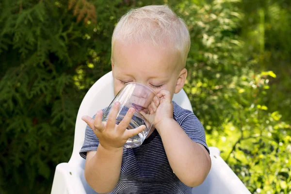 Смешной мокрый мальчик пытается пить воду из стакана самостоятельно — стоковое фото