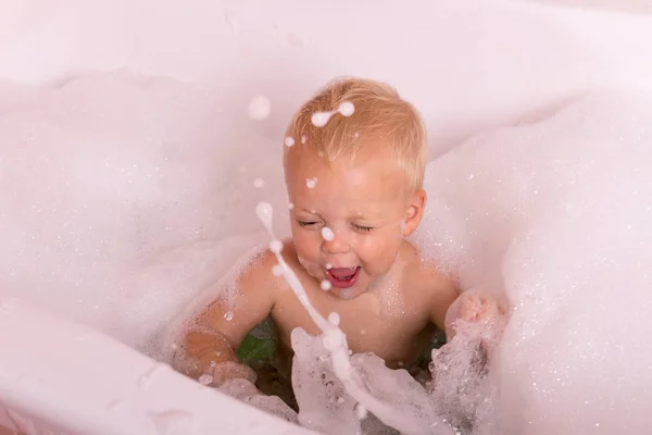 Грайливий малюк бризкає у ванні. Смішний хлопчик грає з білою мильною водою . — стокове фото
