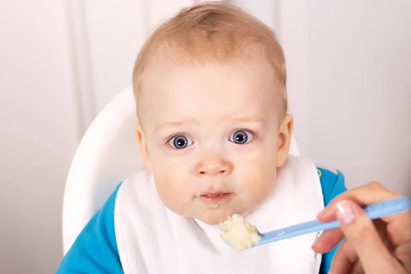 Lindo niño de ojos azules comiendo gachas. hijo de un añoMadre alimentando a su adorable hijo de un año — Foto de Stock