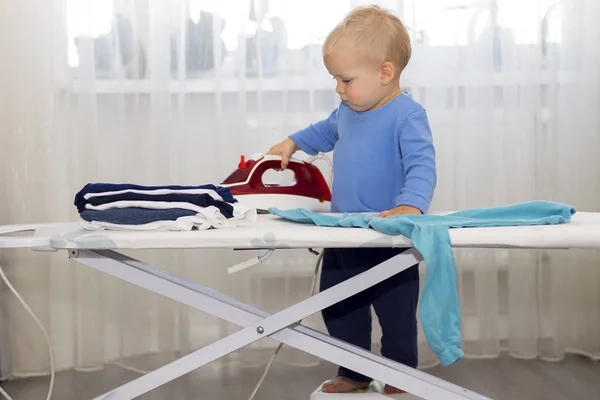 Happy smiling boy ironing clothes. Kid helping with housework. Encouraging Autonomy in children