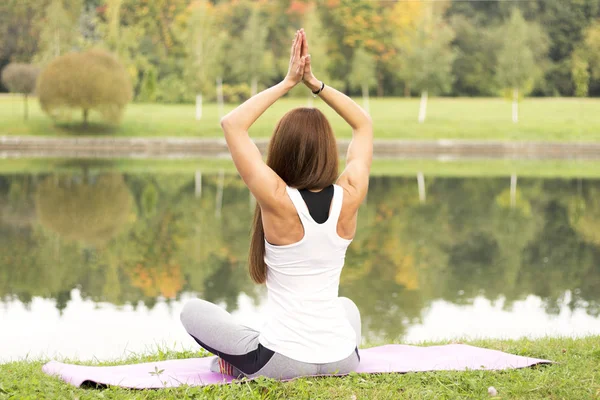 Fitness, sport, yoga and healthy lifestyle concept - young attractive woman meditating in lotus pose on river or lake coast — Stock Photo, Image