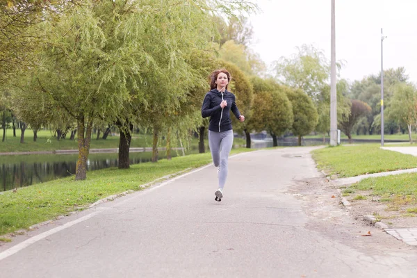 年轻的幸福的女人，在秋天的公园慢跑。跑步健身的女孩 — 图库照片