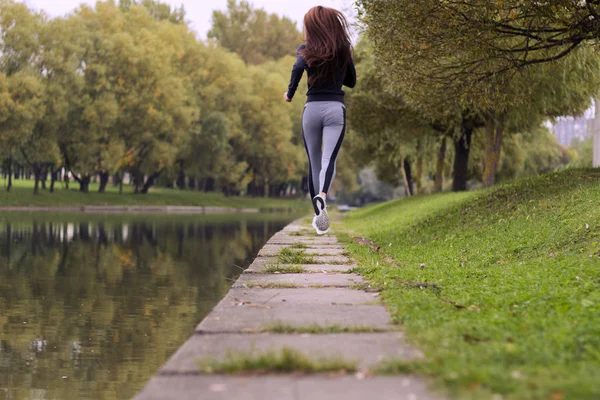 Jeune femme faisant du jogging dans la nature d'automne sur la rive de la rivière. Course Fitness fille vue de dos — Photo