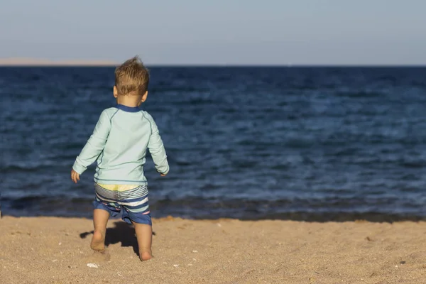 Vista posteriore del bambino in costume da bagno che corre verso il mare. Copia spazio . — Foto Stock