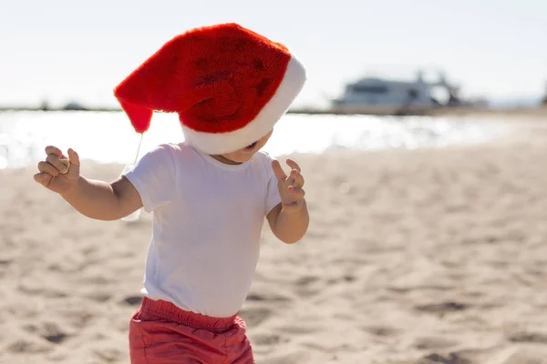 Zabawny mały chłopiec w Santa Boże Narodzenie czerwony kapelusz zabawy na brzegu oceanu — Zdjęcie stockowe