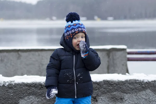 Забавный малыш ест снег. Удивлен новым вкусом. Зимний выстрел — стоковое фото