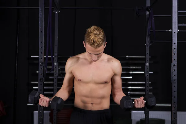 Gros plan portrait d'un jeune homme en forme soulevant des poids dans la salle de gym sur fond sombre . — Photo