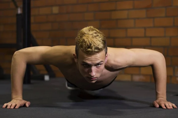 Αθλητής με ένα όμορφο σώμα και ένα γυμνό κορμό κάνει push-ups άσκηση στο πάτωμα. Studio πυροβολήθηκε σε ένα σκοτεινό τόνο. — Φωτογραφία Αρχείου