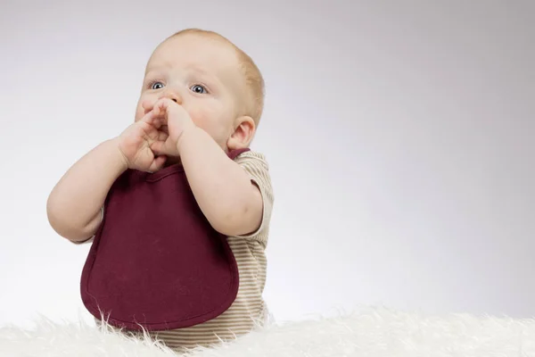 Glada barn baby tittar upp och hålla handflatorna nära munnen. Idé för gratulationskort. Överraskade spädbarn pojke sitter på det vita täcket. Horisontella studio skott. Kopiera utrymme. — Stockfoto